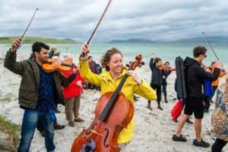 Classical musicians - violinists and cellists - on a beach beside the sea, looking happy