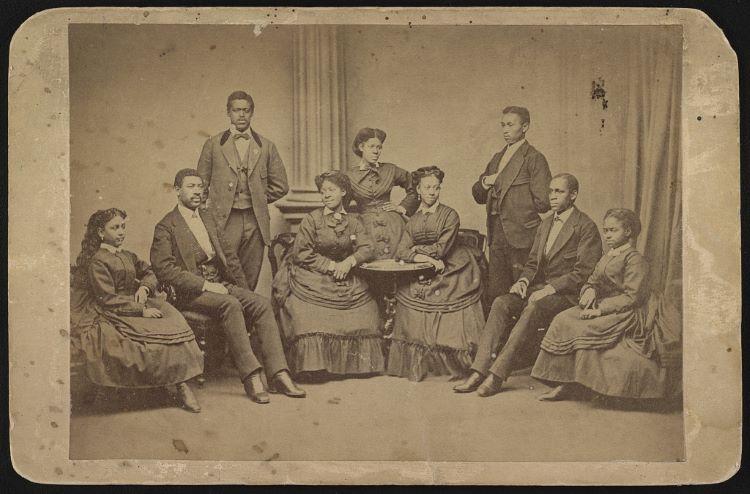 19th century sepia tinted photography of singers from Fisk College, women and men, seated and standing around a harmonium