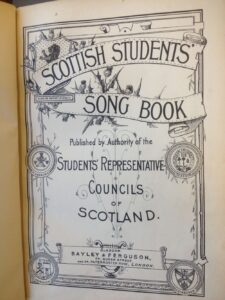 Frontpage showing Scottish Students Song Book with emblems of the Universities and Scottish lion and thistles.