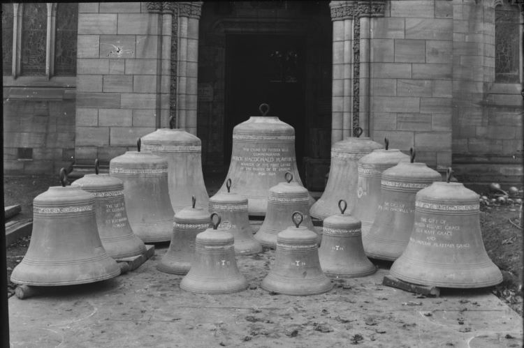A black and white photo with bells of many sizes sitting outside a church door