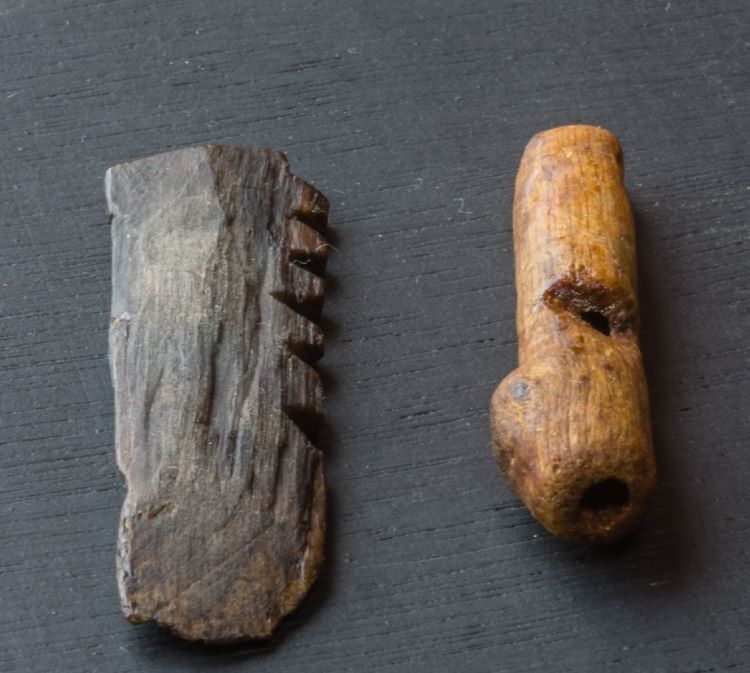 a wooden notched lyre bridge beside a bone whistle