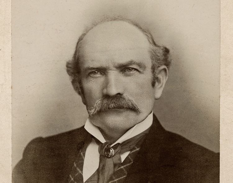 Old photograph of a man with a moustache, sideburns and bald head in formal suit and cravat